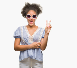 Young afro american woman wearing glasses over isolated background smiling with happy face winking at the camera doing victory sign. Number two.