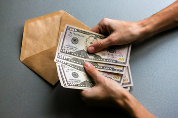 Hands holding fifty  dollar banknotes, envelope in background .