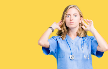 Beautiful young doctor woman wearing medical uniform over isolated background Smiling pulling ears with fingers, funny gesture. Audition problem