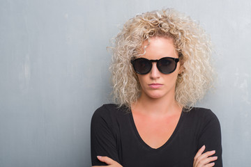 Young blonde woman with curly hair over grunge grey background skeptic and nervous, disapproving...