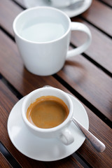 Espresso coffee hot in wooden black background, with spoon and warm water in white glass.