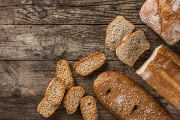 Different fresh bread and spikelets of wheat on rustic wooden background. Creative layout made of bread. Healthy food concept, top view, flat lay, copy space