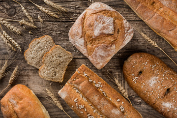 Different fresh bread and spikelets of wheat on rustic wooden background. Creative layout made of bread. Healthy food concept, top view, flat lay, copy space