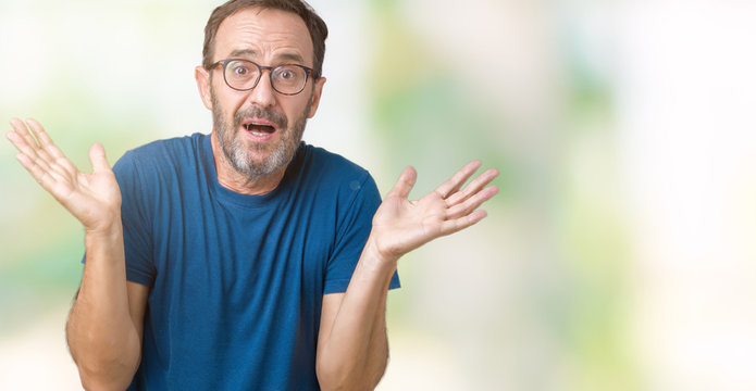 Handsome middle age hoary senior man wearin glasses over isolated background clueless and confused expression with arms and hands raised. Doubt concept.