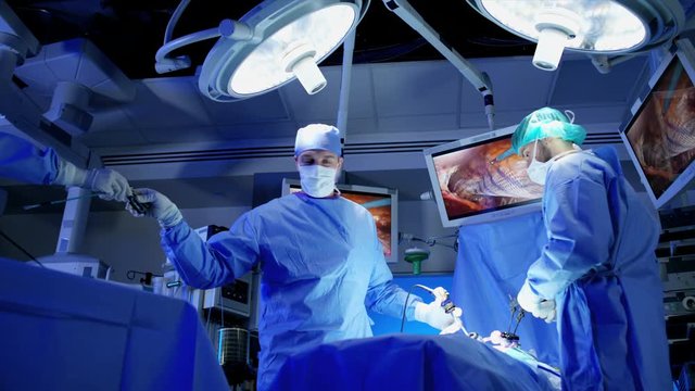Laparoscopy surgical operation transmitted on hospital monitor performed by Caucasian males training as surgeons wearing gloves and scrubs 