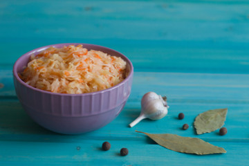 Photo of cabbage salad with carrots in a plate and garlic on a bright blue wooden background.