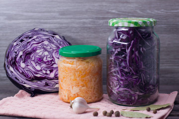 Photo of sauerkraut and carrots in a jar and purple cabbage in a jar on a wooden background.