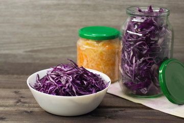 Photo of purple cabbage in a plate and in a jar and sauerkraut on a wooden background.