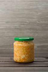 Photo of sauerkraut and carrots in a jar on a wooden background.