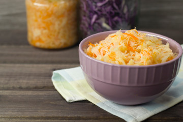 Photo of sauerkraut and carrots in a plate on a wooden background.