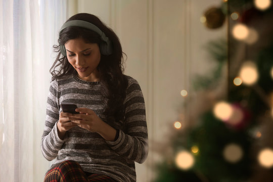 Woman using mobile phone while listening to music during christmas
