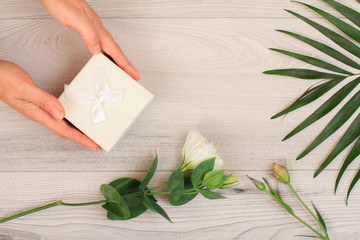 Woman holding a gift box in the hands with flowers on the boards.