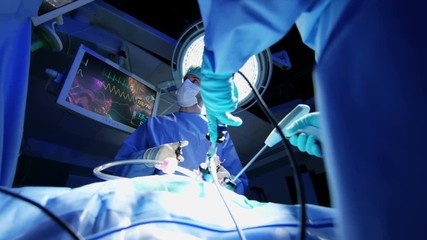 Medical European Caucasian surgical team in scrubs training performing laparoscopic surgery on the patient in sterile operating theater using video camera technology  