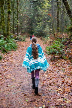 Girl in knitted poncho walks down a leaf strewn path.