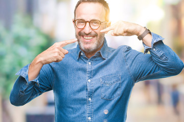 Middle age hoary senior man wearing glasses over isolated background smiling confident showing and pointing with fingers teeth and mouth. Health concept.