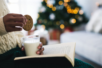 Closeup of a woman eating a cookie and a glass of milk whilst reading a book. 