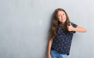 Young hispanic kid over grunge grey wall doing happy thumbs up gesture with hand. Approving expression looking at the camera with showing success.