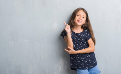 Young hispanic kid over grunge grey wall with a big smile on face, pointing with hand and finger to the side looking at the camera.