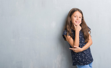 Young hispanic kid over grunge grey wall looking confident at the camera with smile with crossed arms and hand raised on chin. Thinking positive.