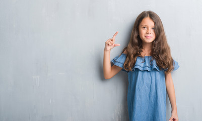 Fototapeta premium Young hispanic kid over grunge grey wall smiling and confident gesturing with hand doing size sign with fingers while looking and the camera. Measure concept.