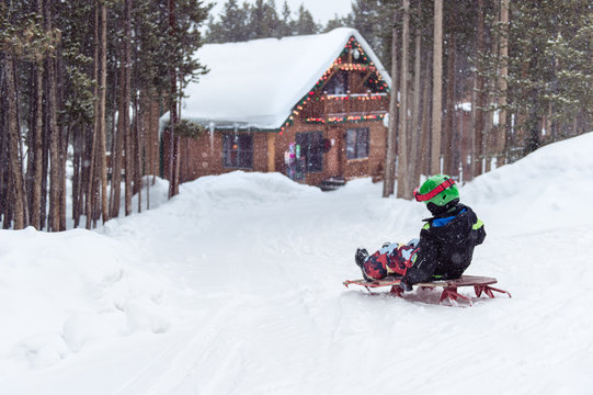 Boy rides a wooden sled down a snow covered driveway