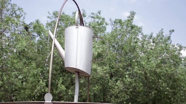 Medium shot, pan around of steel watering can water feature.
