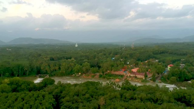 Aerial shot of river flowing between two green forested areas with view of check dam and bridge across river