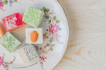 Traditional turkish delight on a plate on white wooden background. Assorted Oriental sweets.