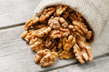 Walnuts in a burlap bag on a wooden gray background.