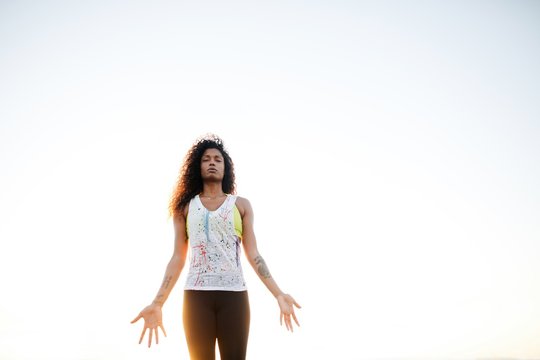 Fit, stylish woman practicing yoga at sunset on grass