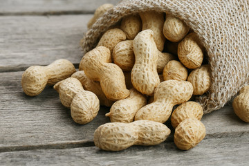 Peanuts in a miniature burlap bag on old, gray wooden surface