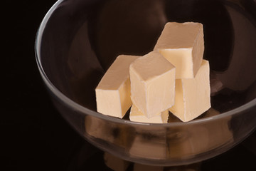 Pieces of butter lie in a glass bowl on a dark background in the studio.