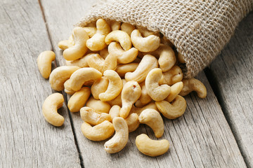 Cashew nuts in burlap bag on wooden gray background . Healthy food