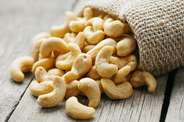 Cashew nuts in burlap bag on wooden gray background . Healthy food