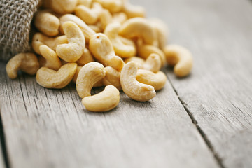 Fototapeta premium Cashew nuts in burlap bag on wooden gray background . Healthy food