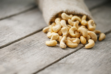 Cashew nuts in burlap bag on wooden gray background . Healthy food
