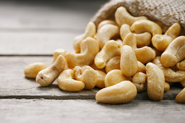 Cashew nuts in burlap bag on wooden gray background . Healthy food