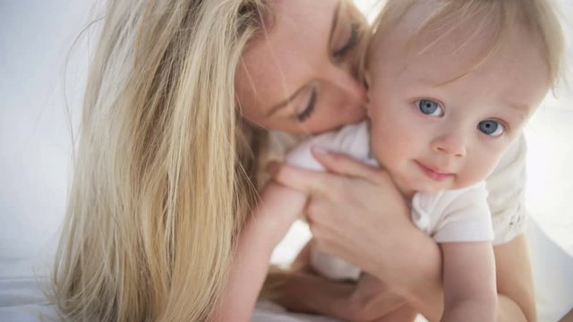 Portrait of cute baby girl with loving mother chilling under the white scarf in the park 