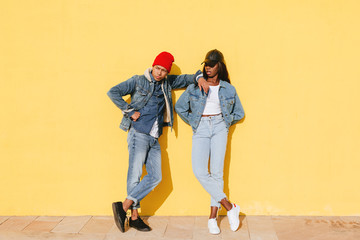 Portrait of cool couple wearing denim clothes in yellow wall. 