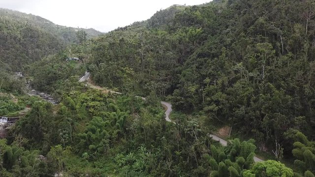 Pulling away and pushing towards a secretive dirt curvy road in the mountains of Puerto Rico near El Ataud Waterfall and revealing the waterfall from the bottom half of the frame.