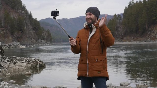 bearded tourist photographs himself on a mobile phone on the bank of a mountain river. slow motion