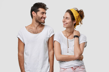 Indoor shot of glad young brother and sister in casual clothes, look with positive expressions, enjoy spare time together, model over white studio wall, have friendly relationships. Two people indoor.