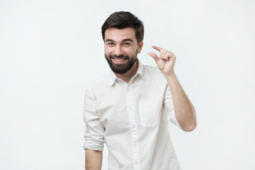 Handsome hispanic man showing something little with hands while gesturing and broadly smiling. He is glad to have a small loan interest rate