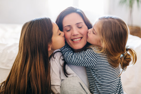 Portrait of daughters kissing her mom at home.