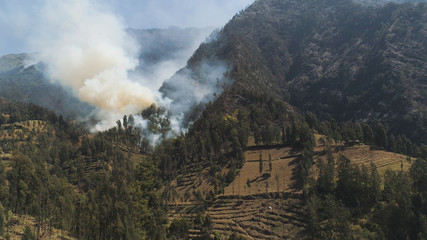 Fototapeta premium fire in mountain forest. aerial view forest fire and smoke on slopes hills. wild fire in mountains in tropical forest, Java Indonesia. natural disaster fire in Southeast Asia