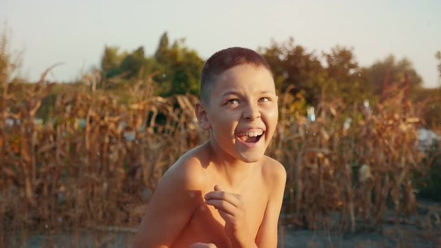 Small boy laughing under a stream of water on a lake bank in summer in slo-mo   