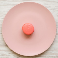 Pink macaroon on a pink plate over white wooden background, top view. Closeup. Flat lay, from above, overhead.