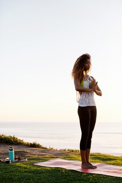 Fit, stylish woman practicing yoga at sunset on grass