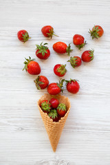 Waffle sweet ice cream cone with strawberries over white wooden background, top view. Flat lay, from above. Close-up.