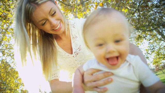Portrait of cute blonde baby boy bouncing up and down outdoors while his loving mom holds him 